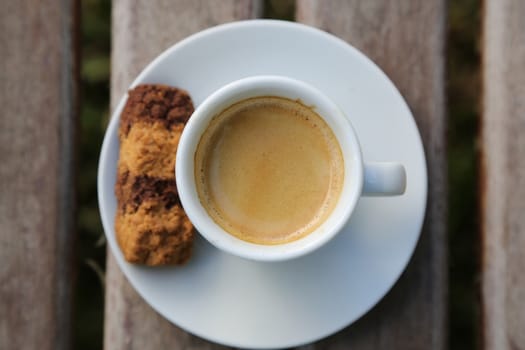 A cup of Italian espresso with a biscuit on the plate placed on the wooden surface - top view