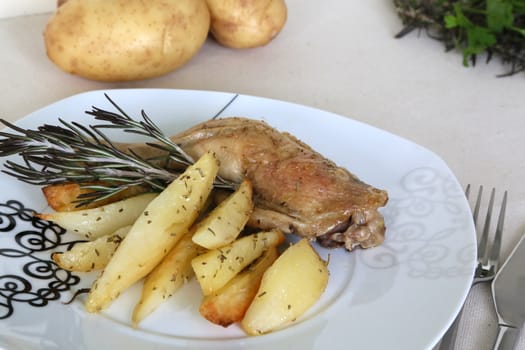 A plate with baked potatoes, chicken, fresh parsley with a fork and knife on the table