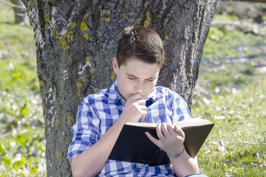 Young boy reading a book in the woods with shallow depth of field and copy space