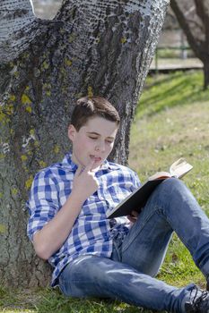 Young boy reading a book in the woods with shallow depth of field and copy space