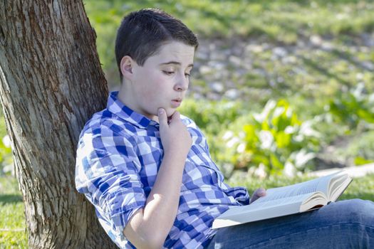 Young boy reading a book in the woods with shallow depth of field and copy space