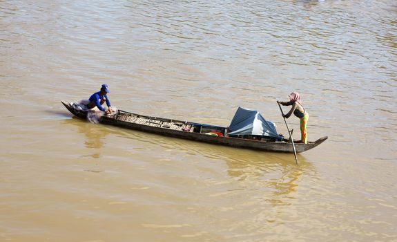 DONG THAP, VIET NAM- NOV 12: Couple of fisherman working on river, woman  rowing the wooden boat, the man pick up the fishing net on the boat in Dong Thap, VietNam on Nov 12, 2013