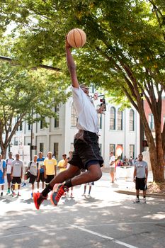 Athens, GA, USA - August 24, 2013:  A young man leaps to slam dunk the basketball in an impromptu dunk competition, in between games at a 3-on-3 basketball tournament held in the streets of downtown Athens.