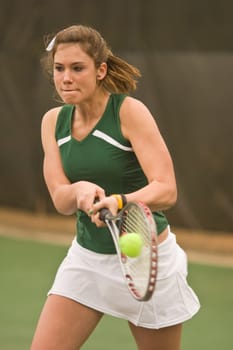 A female high school tennis player hits a powerful two-handed backhand during a match.