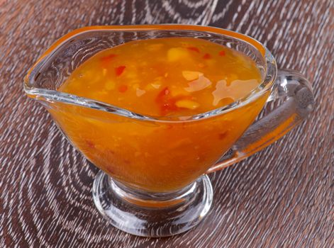 Thai Spicy Sauce in Glass Gravy Boat isolated on Wooden background
