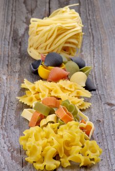 Arrangement of Spaghetti Nest, Pasta Shells, Bow Tie Pasta, Heart Shaped Pasta and Fusillini In a Row on Rustic Wooden background