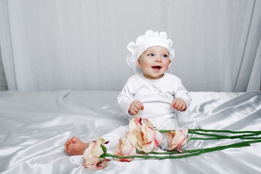 Little girl sitting on silk sheets lie at the feet of flowers