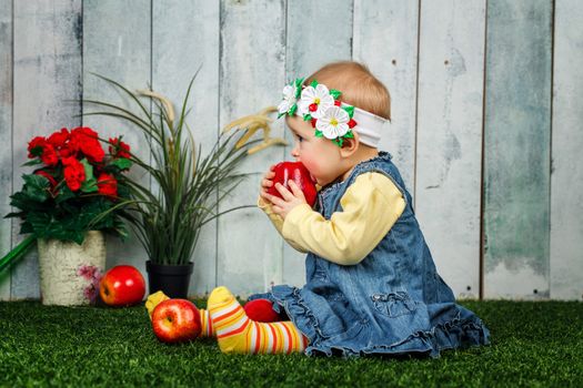 Little girl in the backyard sits on a lawn and eats an apple