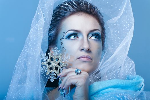 Girl with scenic make-up of the Snow Queen is holding a snowflake shot closeup
