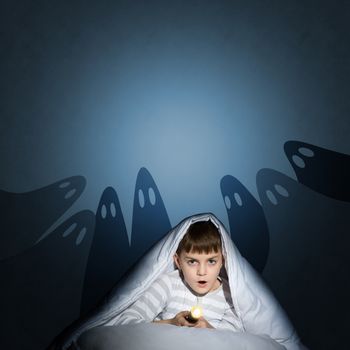 image of a boy under the covers with a flashlight the night afraid of ghosts