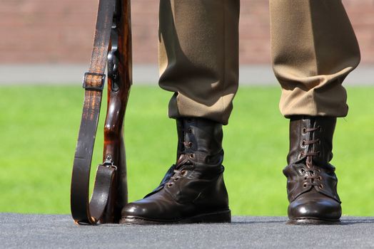 A soldier stands next to his feet and rifle on guard.