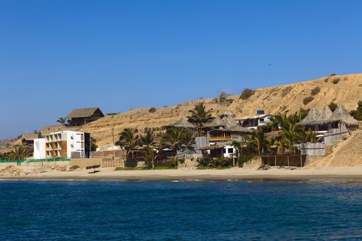 MANCORA, PERU - AUGUST 17, 2013: Thatched roof accomodation with palm trees and a modern building along the sandy beach on August 17, 2013 in Mancora, Peru. Mancora is one of the most popular beach towns of Peru. 