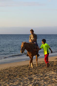 MANCORA, PERU - AUGUST 20, 2013: Unidentified young man and child on horseback, with unidentified boy walking along the horse on the beach on August 20, 2013 in Mancora, Peru. Mancora is a popular beach town in Peru for both Peruvian and foreign tourists.   