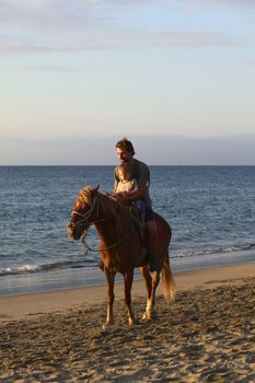 MANCORA, PERU - AUGUST 20, 2013: Unidentified young man and child on horseback on the beach on August 20, 2013 in Mancora, Peru. Mancora is a popular beach town in Northern Peru both for Peruvian and foreign tourists