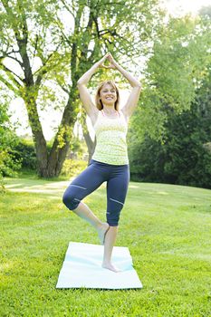 Female fitness instructor doing yoga tree or vrksasana pose in green park