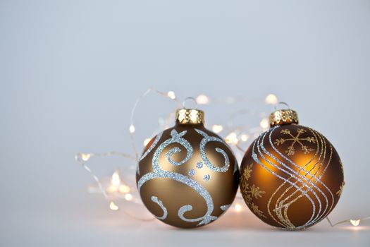 Two gold Christmas decorations and decorative lights on gray background with copy space