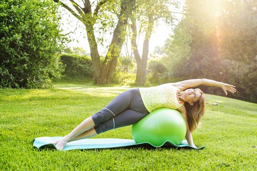 Female fitness instructor using yoga exercise ball  outdoors in morning sunshine
