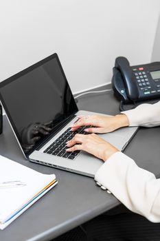 Female hands typing on laptop keyboard at office desk