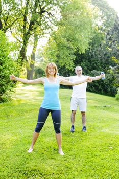 Female fitness instructor exercising with middle aged man outdoors in green park