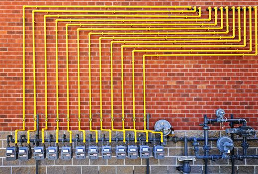 Row of natural gas meters with yellow pipes on building brick wall