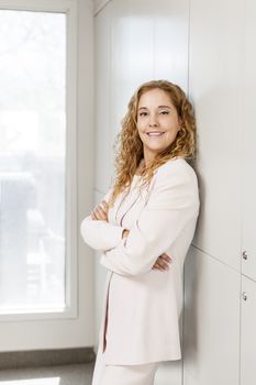 Confident business woman standing in office hallway with arms crossed