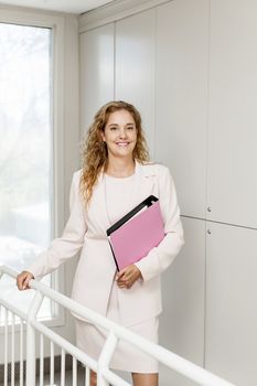 Smiling powerful business woman standing in office hallway holding binder