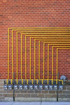 Row of natural gas meters with yellow pipes on building brick wall