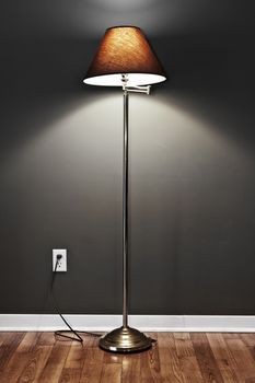 Tall floor lamp with metal base and dark lampshade on hardwood flooring in room
