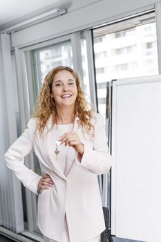 Smiling female real estate agent offering keys standing with blank flip chart