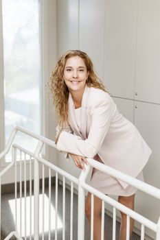 Smiling proud business woman standing in office hallway leaning on railing