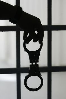 Man hand with handcuffs behind bars