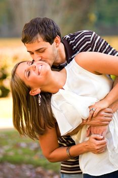A young couple in love playfully embrace in a pretty wooded area.