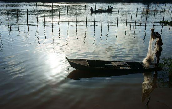 silhouette  's fisherman standing on row boat, pick up the net, repair for fishing to catch fish on river at morning in flood season 