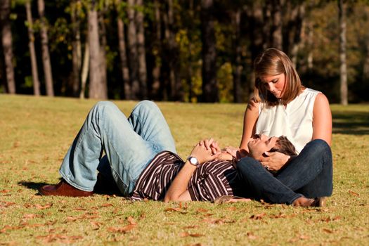 A young couple in love share an intimate moment while laying on a grassy field. 