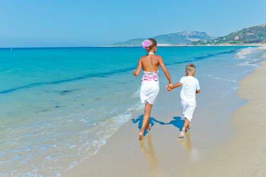 Back view of adorable happy boy and girl runs along beach vacation