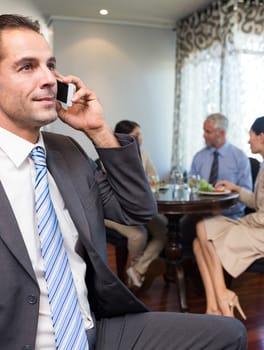 Businessman using cellphone with colleagues having meal in background at the table