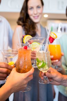 Closeup of cheerful people toasting cocktails over blurred background