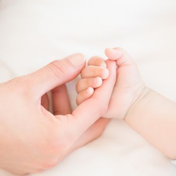 Mother holding baby sons hand at home in bedroom