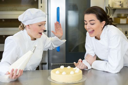 Confectioner apprentice nibbling whipped cream from cake in bakery