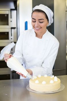 Female baker or confectioner prepares cake with whipped cream