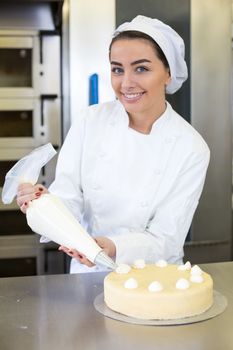 Female baker or confectioner prepares cake with whipped cream
