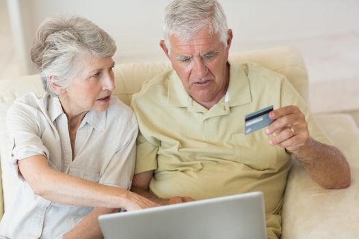 Senior couple using the laptop together to shop online at home in the living room