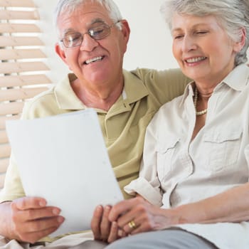Senior couple looking at document together on the couch at home in the living room