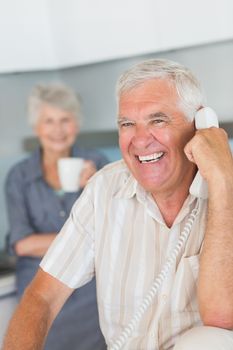 Happy senior man on the phone at home in the kitchen