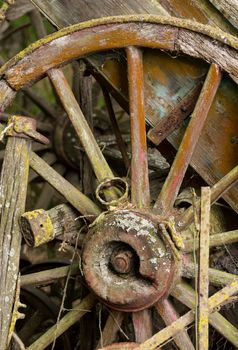 Old wooden cartwheel against a ruined wood cart or buggy in detailed close up