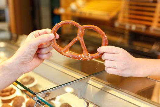 shopkeeper in baker's shop gives pretzel to customer