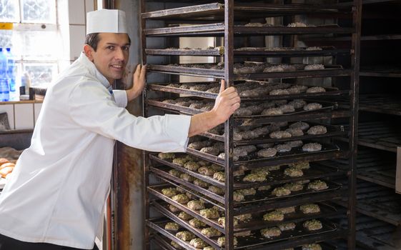 Baker putting a rack of bread into the oven in bakery or bakehouse