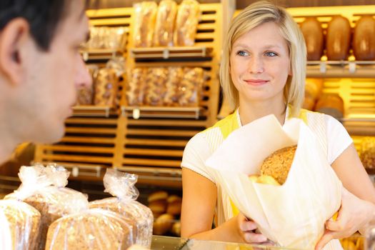 Bakery shopkeeper hands bag of bread over to customer