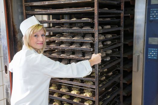 Baker putting a rack of bread into the oven in bakery or bakehouse