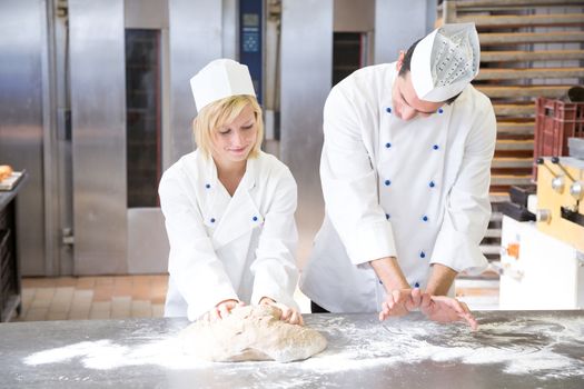 Baker instructing apprentice how to knead dough properly